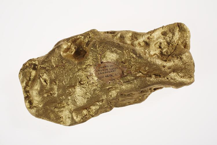 Gold nugget replica containing a circle with writing on it.
