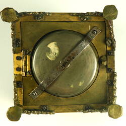Decorative table clock, square gilded brass case on four feet. Underside view.