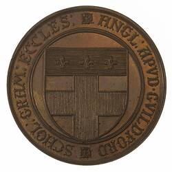Round medal with shield in centre and text around edge.