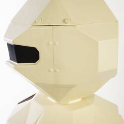 Detail of head of cream plastic robot with angular human-like shape, ie. head, shoulders, waist and legs. Black plastic features.