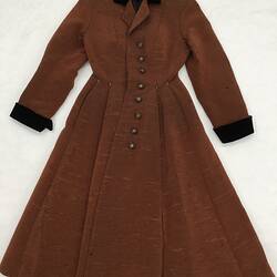 Long coat made from a reddish brown ribbed fabric. Laid flat.