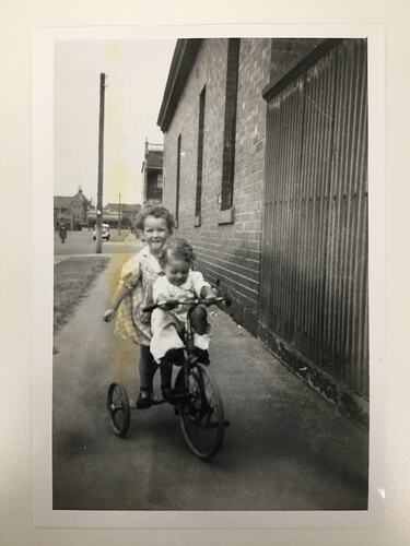 Children with tricycle on street.