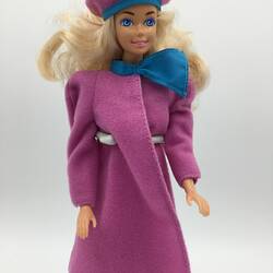 Barbie doll with blonde hair wearing pink with blue trim coat and hat.