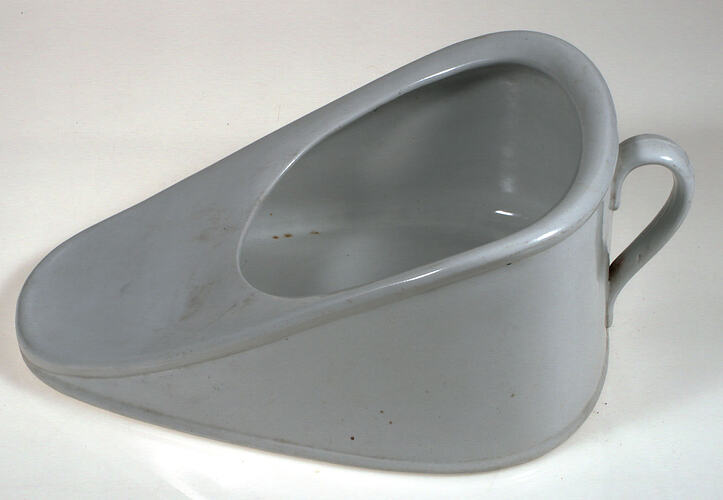 Ceramic bedpan in the shape of a slipper with a handle.