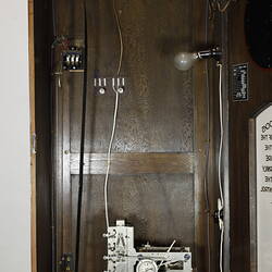 Wooden clock detail with top cabinet door open. Mechanism visible.