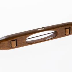 Wooden shuttle with a piece of thick wire through cut out centre. Two wooden rollers underneath shuttle.