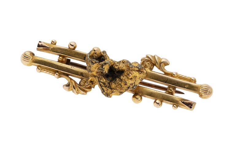 Gold double bar brooch with decorative detailing. Features small natural nugget in centre.