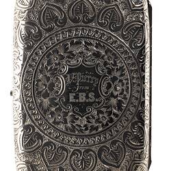 Heavily engraved silver cigarette case with central text. Rectangular with rounded corners.