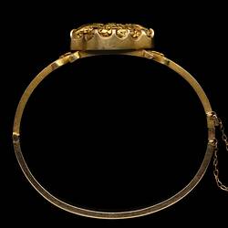 Profile of gold bangle (bracelet) featuring a large gold nugget. Fine chain at right.