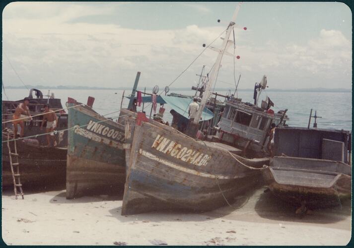 Four beached refugee boats on the sand. Ocean behind them.