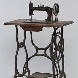 Sewing machine fitted to a metal frame with a wooden bench.