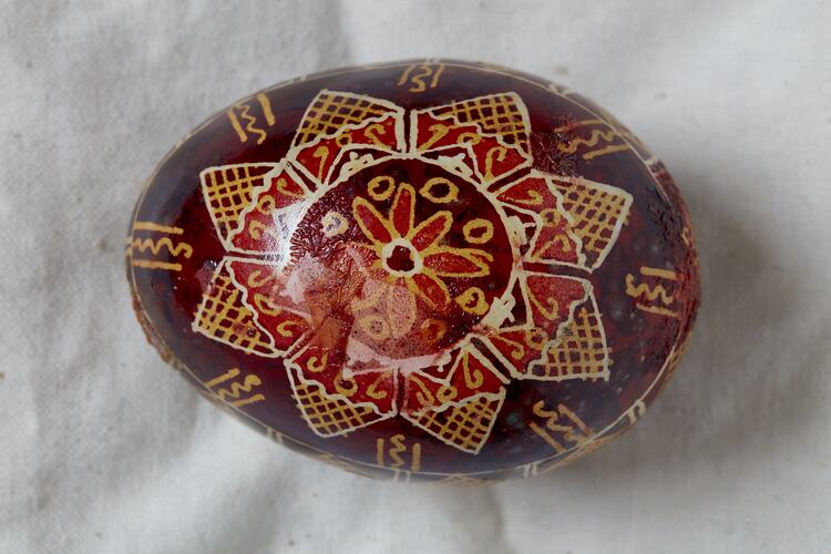 Egg, hand painted on a brown background with yellow, red and white star design at the centre of the egg.