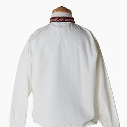 Back of white long sleeve shirt. Red geometric patterned band embroidered at cuffs and collar.