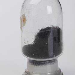 Domed cylindrical jar containing black stringy botanical sample.