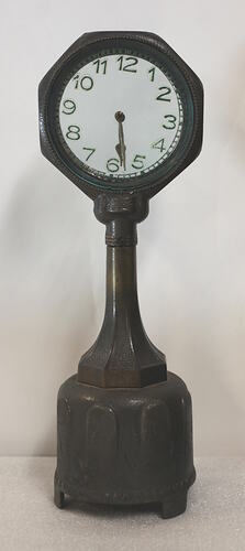 Clock with clear glass face on dark green painted stand.