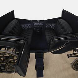 Interior view of black coach with four rubber tyres. Yellow and brown lining, and the Australian coat of arms on each door.