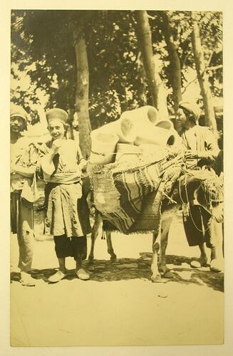 Three Arab men with a donkey, which has pots tied to its back.