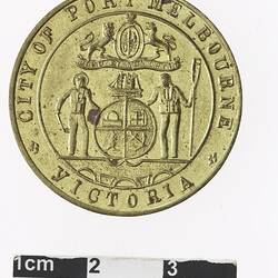 Round gold coloured medal with coat of arms and text surrounding.
