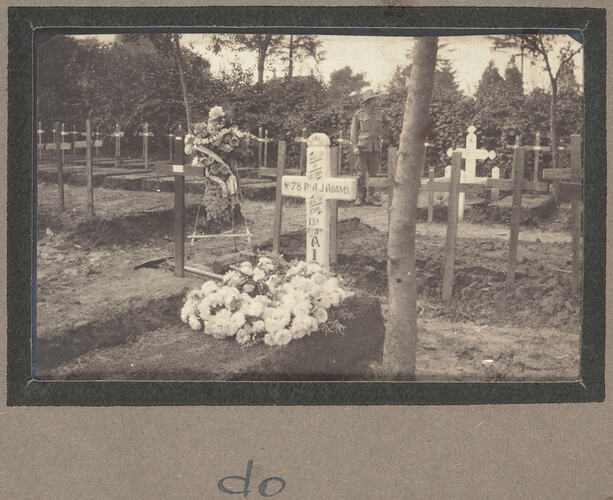 Grave with cross shaped marker covered in writing and two flower arrangements in a graveyard.