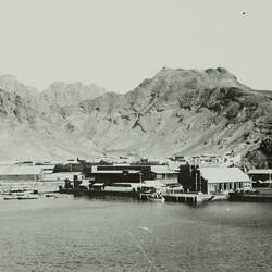 Port with a number of boats and buildings around the waters edge, surrounded by mountains.