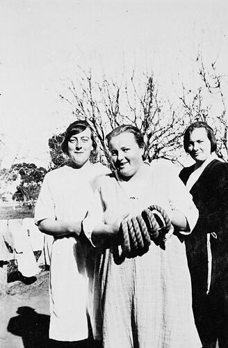 Three women posing outdoors, the middle woman holds quoits.