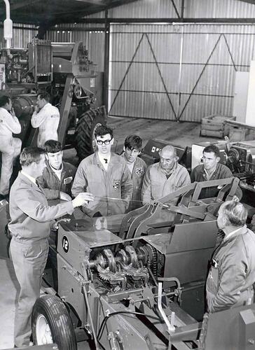 Group of men stand next to machine in workshop.