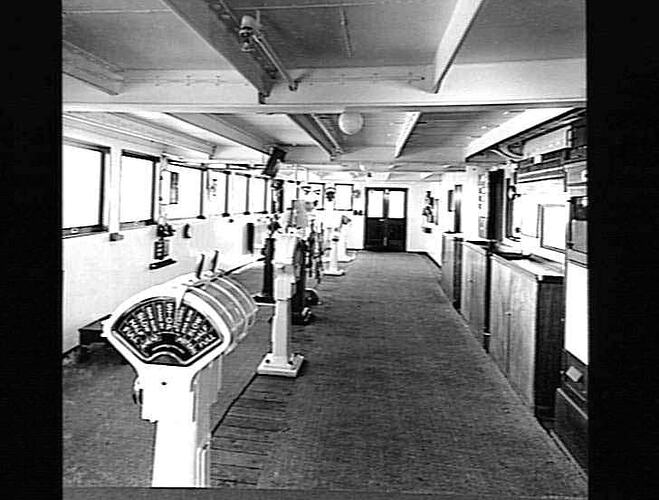 Ship interior. Wheel house. Free-standing equipment in centre and windows at left.