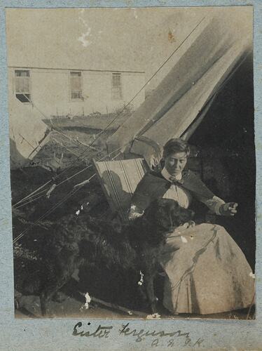 Woman sitting in deck chair in front of tent, next to large dog.