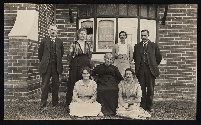 Monochrome photograph of a group near a house.