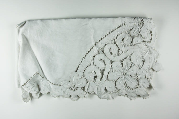 Folded detail of white cutwork embroidery.