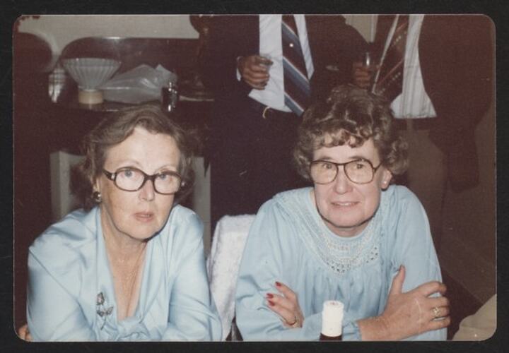 Two women in blue blouses and glasses.
