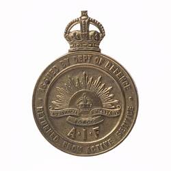 Metal badge with rising sun surrounded by text and crown above.