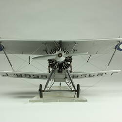 Silver model biplane model with red, white, blue rondels on wings and fuselage. Silver propeller. Back view.