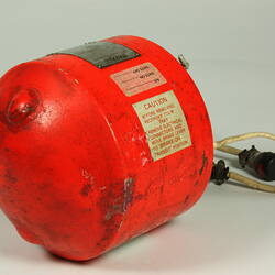 Red cylindrical container with two electrical cords at one end.