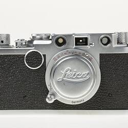 Black camera with metal trim, cap, lens, dials at top corners.