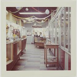 Interior of camera shop with two females standing behind a counter at rear.