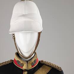 Detail of navy officer's jacket with gold sash, epaulettes. Brass buttons. Red and gold collar, white helmet.