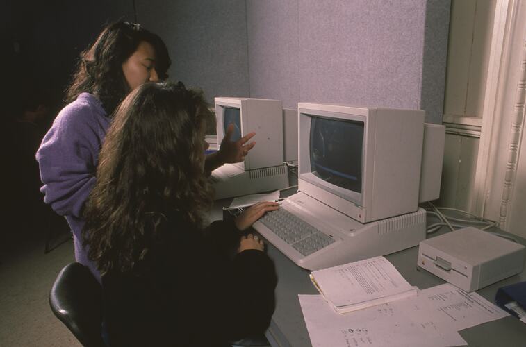 Two young women working together on a computer.