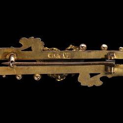 Back of gold double bar brooch with decorative detailing. Front features small natural nugget in centre.