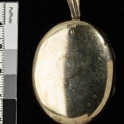 Plain back of polished gold oval locket with loop at top.
