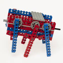 Red, blue and grey LEGO robot with three legs either side. Left profile.