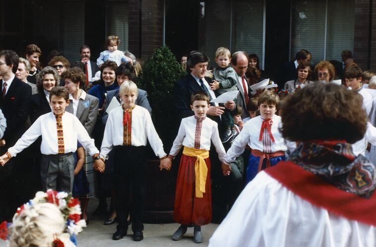 Scene of children wearing traditional Ukrainian dress holding hands and dancing side by side. Crowd behind them.