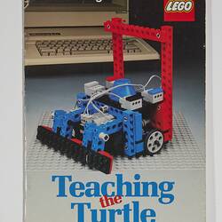 Front cover with LEGO build. Blue and red, grey base. Wheeled, grey cable. Text above, below. Computer behind.