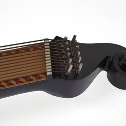 Detail of timber stringed instrument. Pale wood neck with zig zag pattern on edges. Stylised curved black laquered head stock. 61 strings in varied thickness.