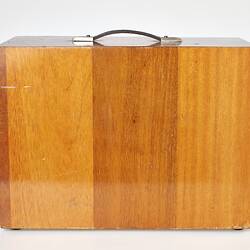 Side view of rectangular wooden box with handle on top.
