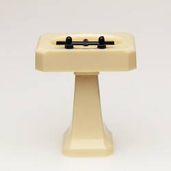 Toy bathroom sink made of cream coloured moulded plastic. Two faucets. Back.