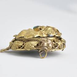 Round gold brooch with gold border and green paste. Profile view.