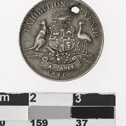 Round silver coloured medal with coat of arms, text above.