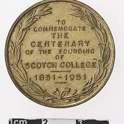 Round gold coloured medal with text, wreath surrounding.