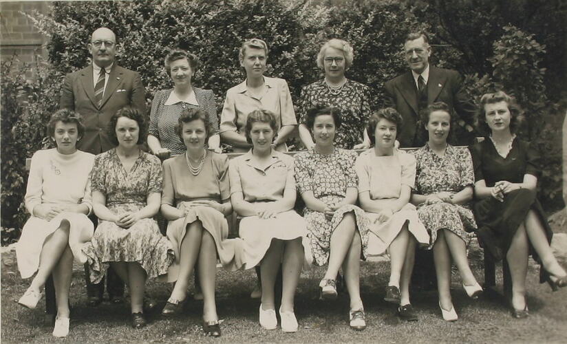 Group of 11 women and 2 men posing in garden setting.